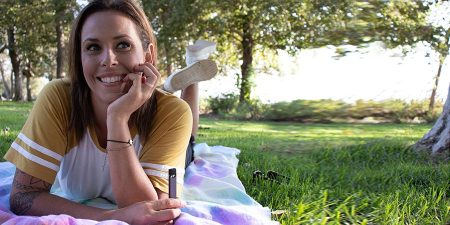 a woman holding a vape device while having a picnic outdoors